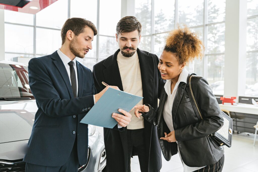 Car Buying Service Three business professionals discussing car purchase details inside a modern dealership.